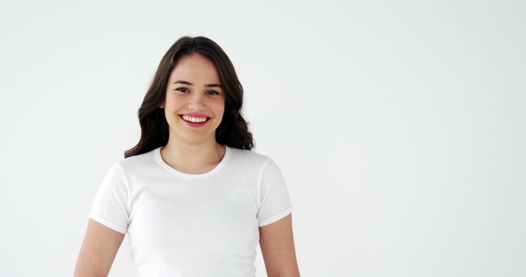 Smiling Young Woman in White T-Shirt Standing Against White Background - Free Images, Stock Photos and Pictures on Pikwizard.com