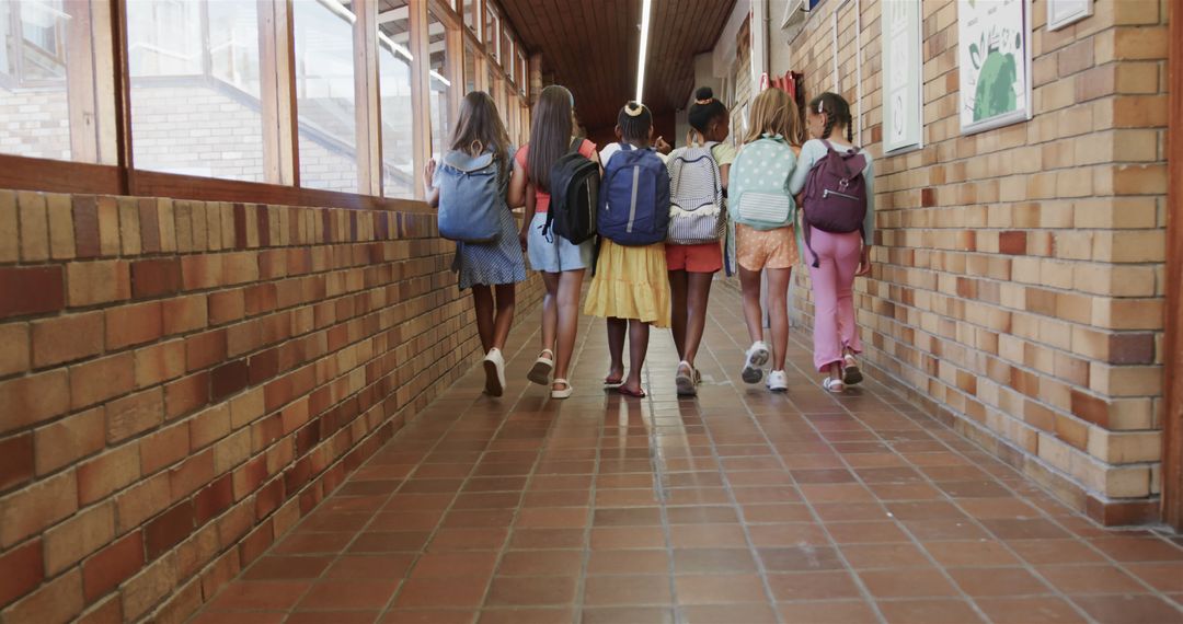 Diverse Elementary Schoolgirls Walking in Corridor with Backpacks