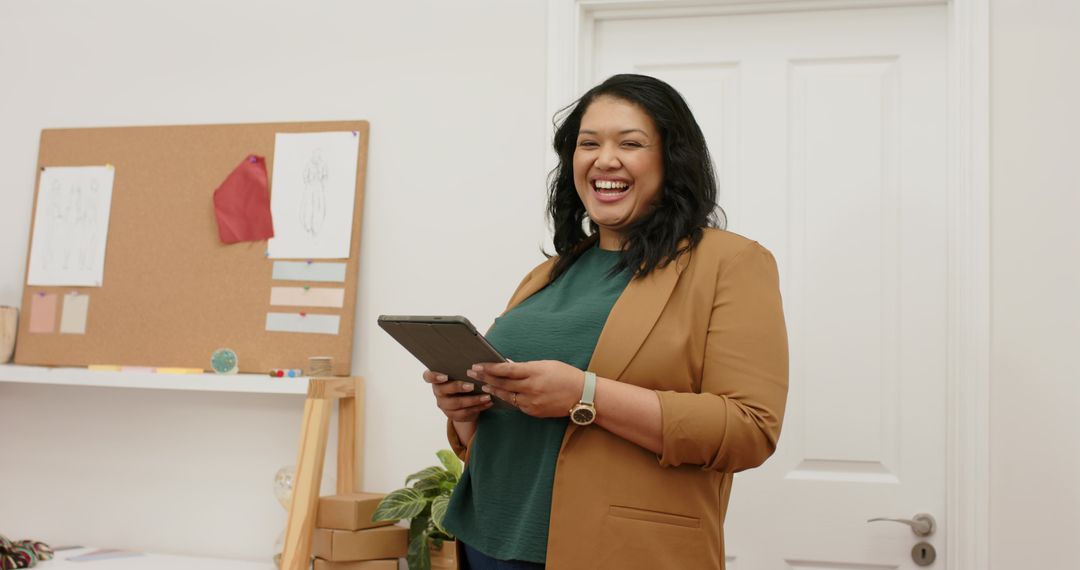 Laughing creative entrepreneur holding tablet in modern minimalist studio workspace