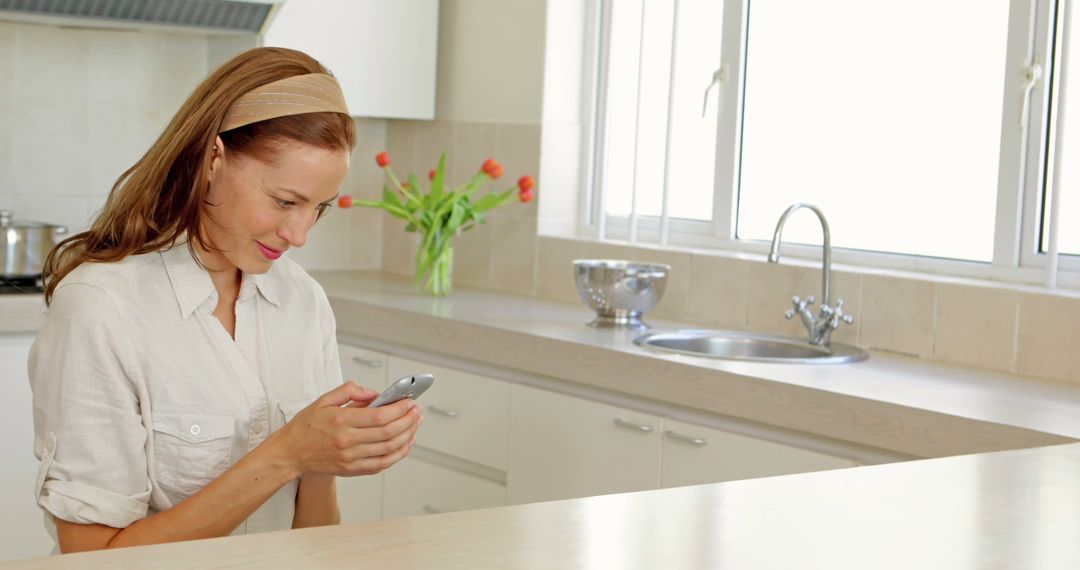 Woman Using Smartphone in Modern Kitchen with Flowers in Background - Free Images, Stock Photos and Pictures on Pikwizard.com