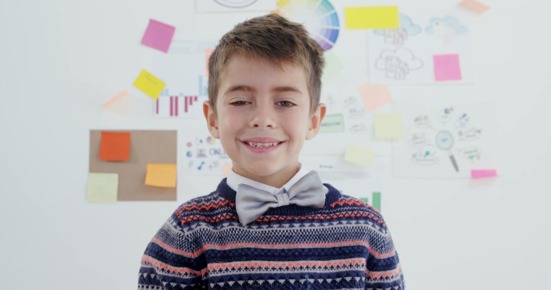 Smiling Boy in Sweater and Bow Tie in Front of Creative Wall Workspace - Free Images, Stock Photos and Pictures on Pikwizard.com