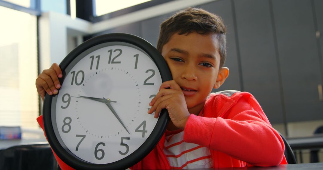 Young Boy Holding Wall Clock in Classroom Learning Time Management