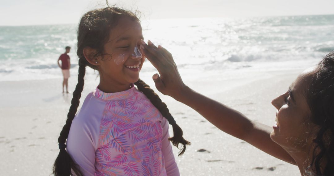 Mother Applying Sun Cream on Smiling Daughter's Nose at Beach