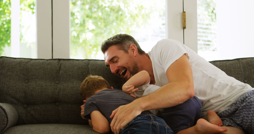 Father and Son Laughing and Playing on Couch at Home - Free Images, Stock Photos and Pictures on Pikwizard.com