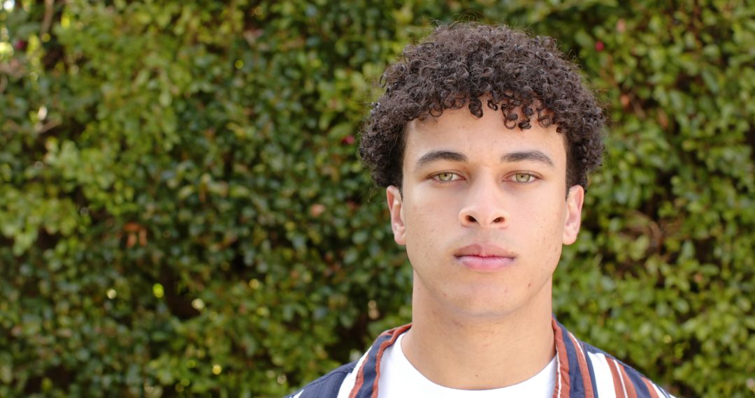 Serious Young Man with Curly Hair Standing Outdoors - Free Images, Stock Photos and Pictures on Pikwizard.com