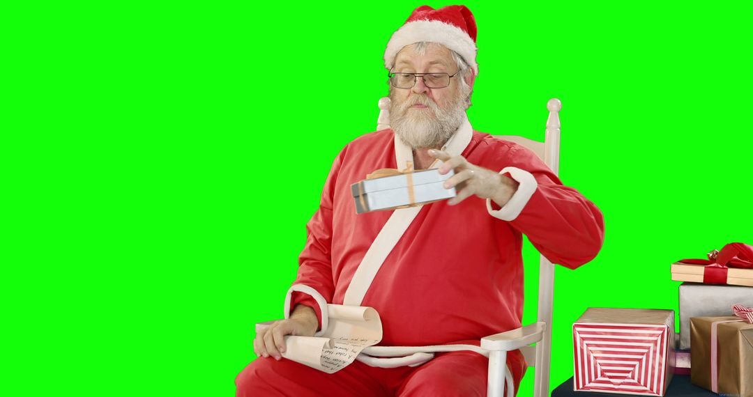 Santa Claus Reviewing Gift List While Holding Present on Green Screen - Free Images, Stock Photos and Pictures on Pikwizard.com