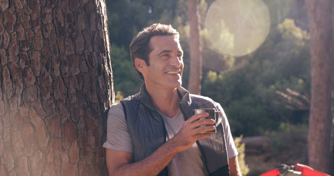 Man Enjoying Coffee in Forest, Leaning Against Tree in Sunlight - Free Images, Stock Photos and Pictures on Pikwizard.com