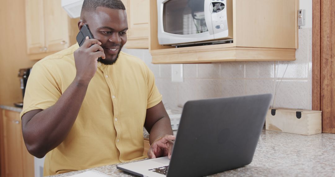 Smiling Man Talking on Phone and Using Laptop in Kitchen - Free Images, Stock Photos and Pictures on Pikwizard.com