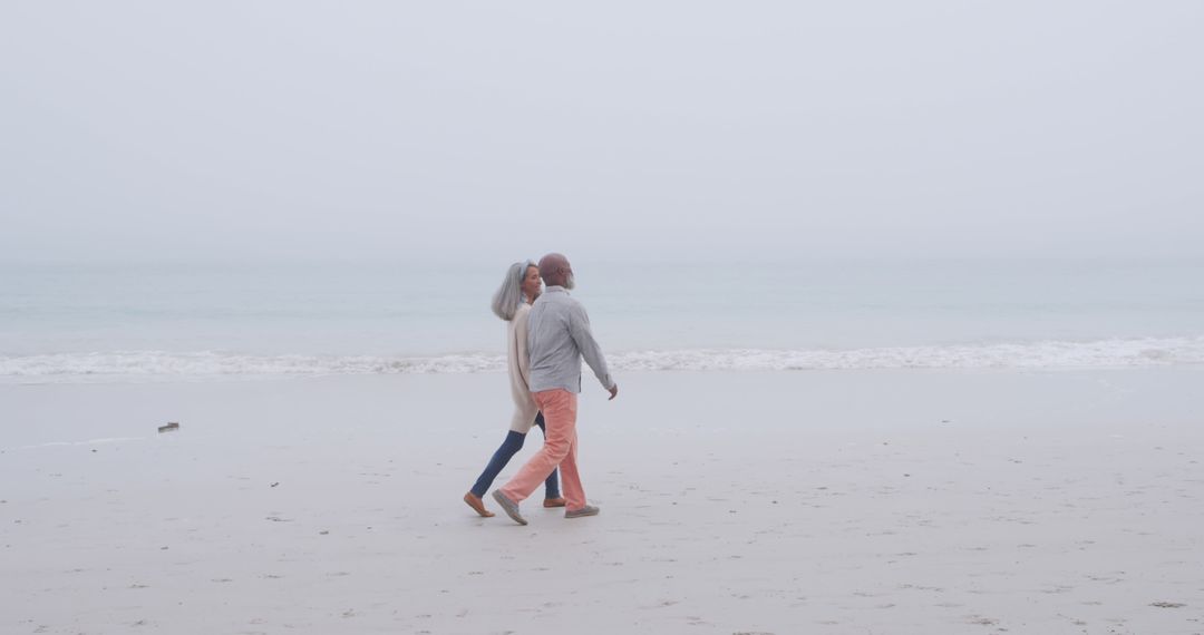 Elderly Couple Enjoying Leisurely Walk on Misty Beach - Free Images, Stock Photos and Pictures on Pikwizard.com