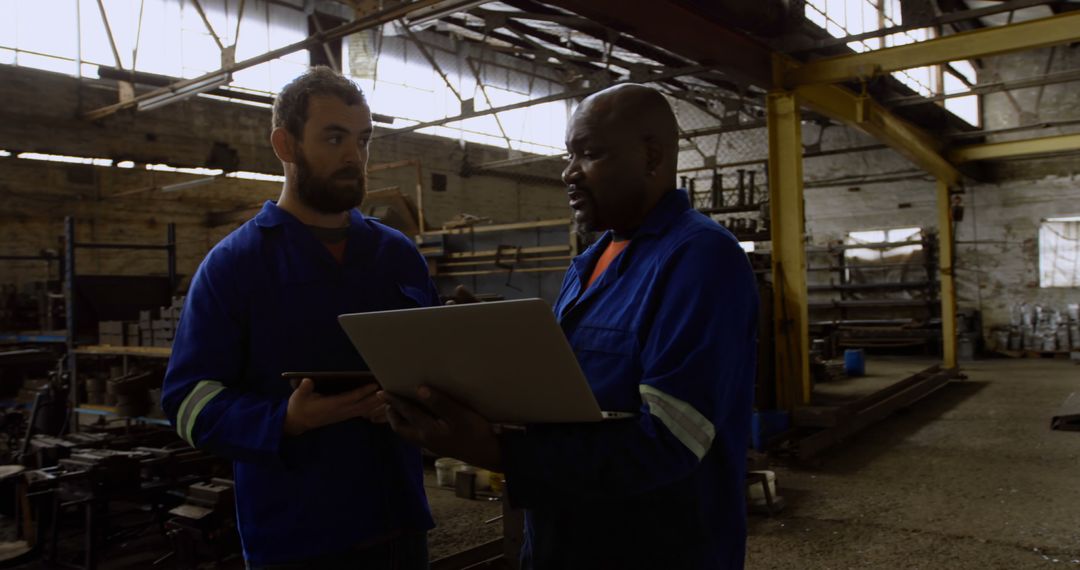 Two Factory Workers Discussing Projects Inside Industrial Warehouse - Free Images, Stock Photos and Pictures on Pikwizard.com