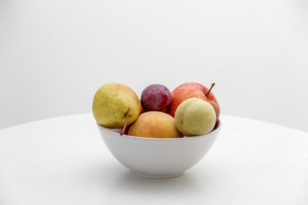 Displaying mixed fruit bowl with pears apples peaches and plum on clean white background