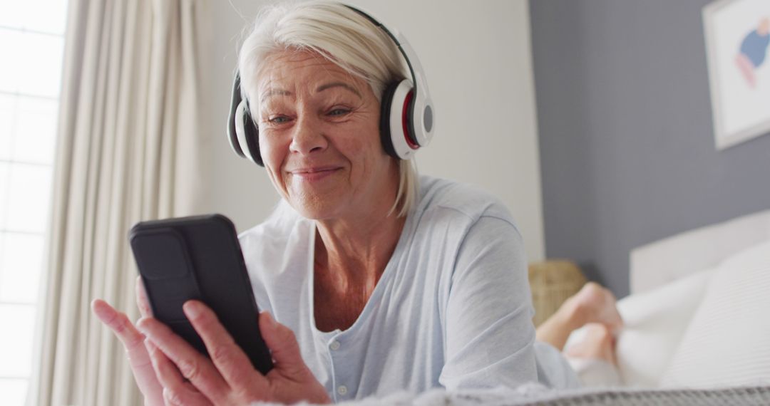 Elderly woman enjoying music on smartphone with headphones at home - Free Images, Stock Photos and Pictures on Pikwizard.com