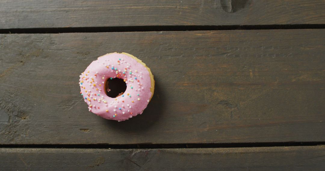 Pink Icing Donut with Sprinkles on Rustic Wood Background