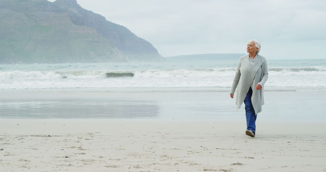 Senior Woman Walking on Beach in Overcast Weather - Free Images, Stock Photos and Pictures on Pikwizard.com