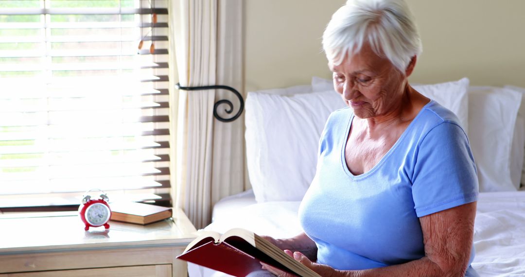 Senior Woman Reading Book on Bed Near Window - Free Images, Stock Photos and Pictures on Pikwizard.com