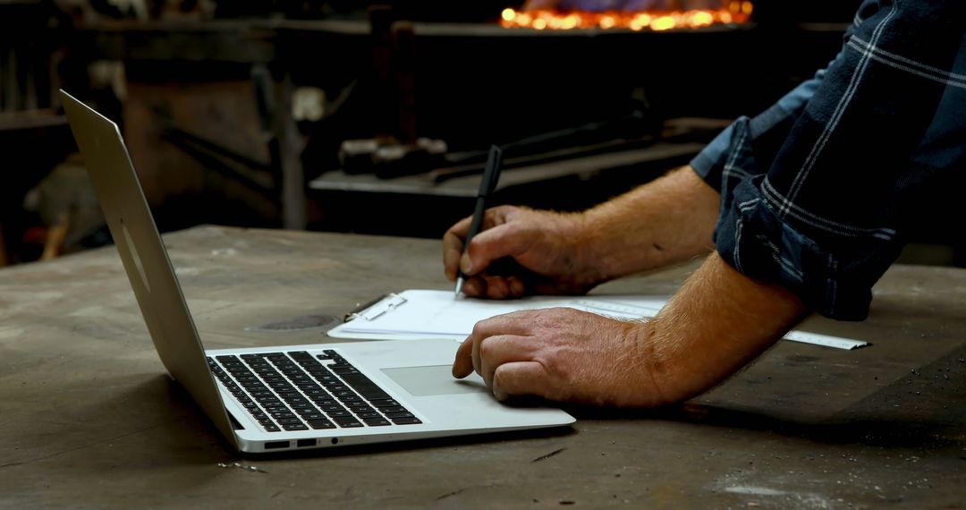 Blacksmith Taking Notes with Laptop in Workshop - Free Images, Stock Photos and Pictures on Pikwizard.com