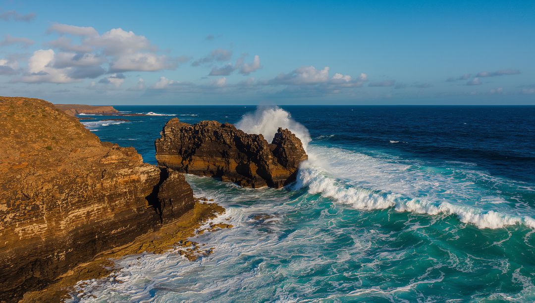 Waves Crashing Against Rugged Cliffs in Vibrant Blue Sea