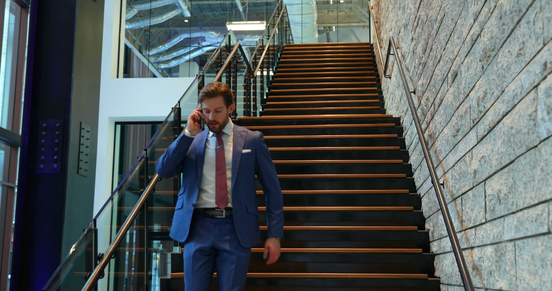 Businessman Talking on Phone While Walking Downstairs in Modern Office Building - Free Images, Stock Photos and Pictures on Pikwizard.com