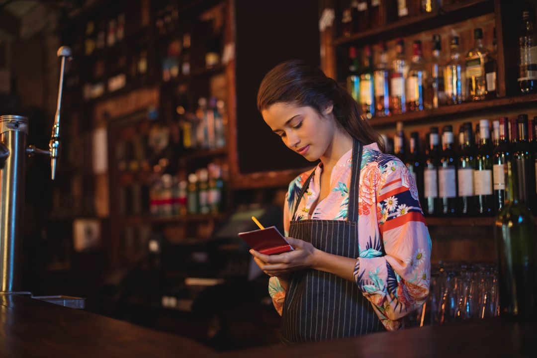 Female Bartender Writing in Notepad at Rustic Bar Counter