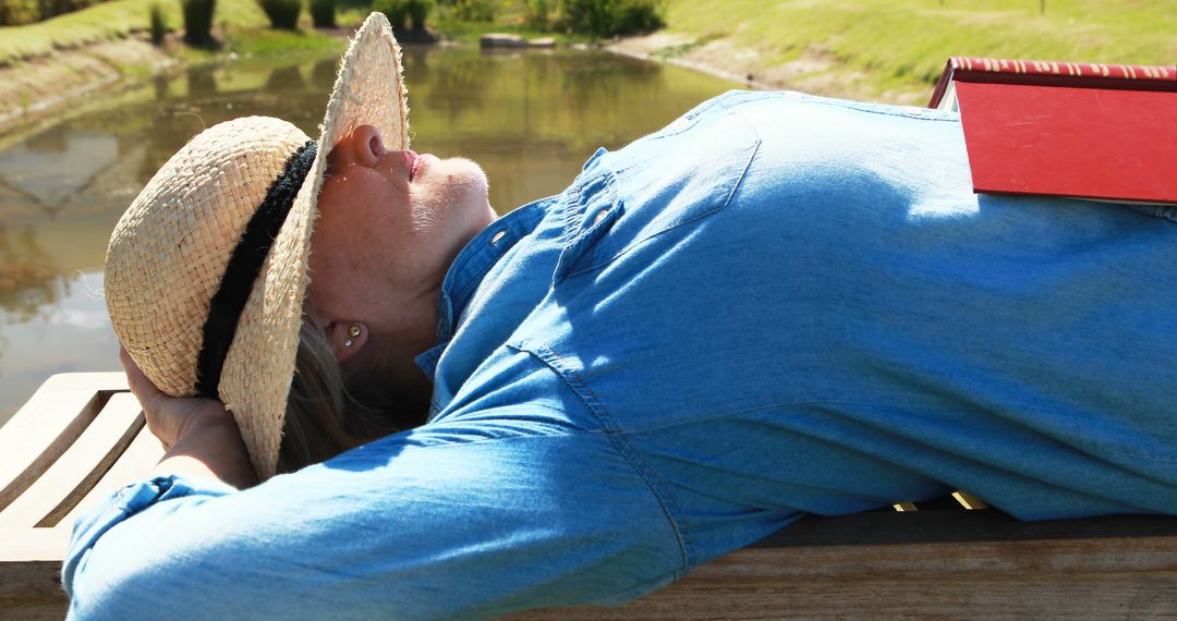 Woman Relaxing Outdoors by Lake with Book in Shade Hat Enjoying Nature - Free Images, Stock Photos and Pictures on Pikwizard.com