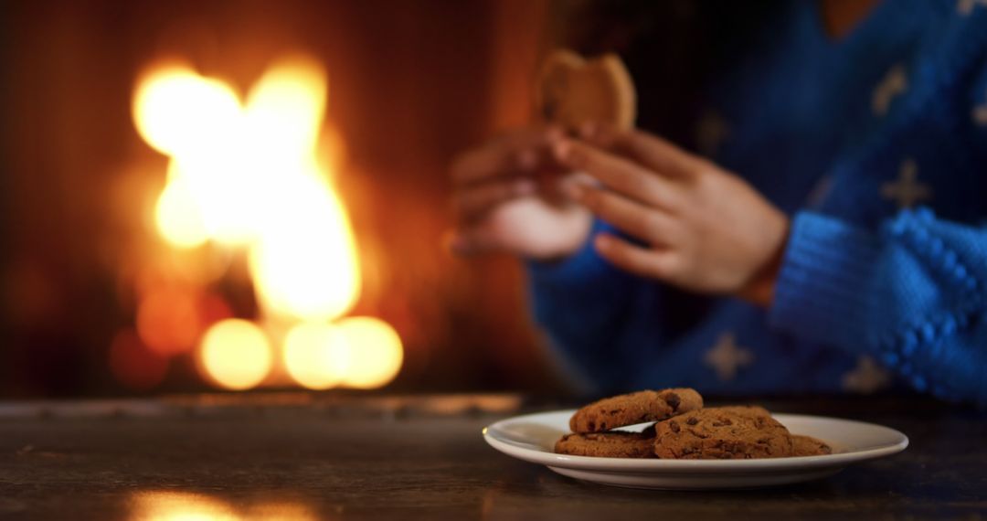 Person Enjoying Chocolate Chip Cookies in Cozy Fireplace Ambience - Free Images, Stock Photos and Pictures on Pikwizard.com