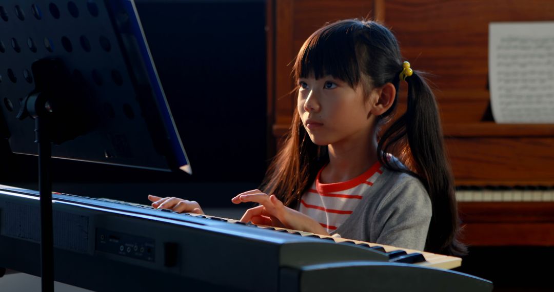 Focused Girl Practicing Piano with Music Sheet in Background - Free Images, Stock Photos and Pictures on Pikwizard.com