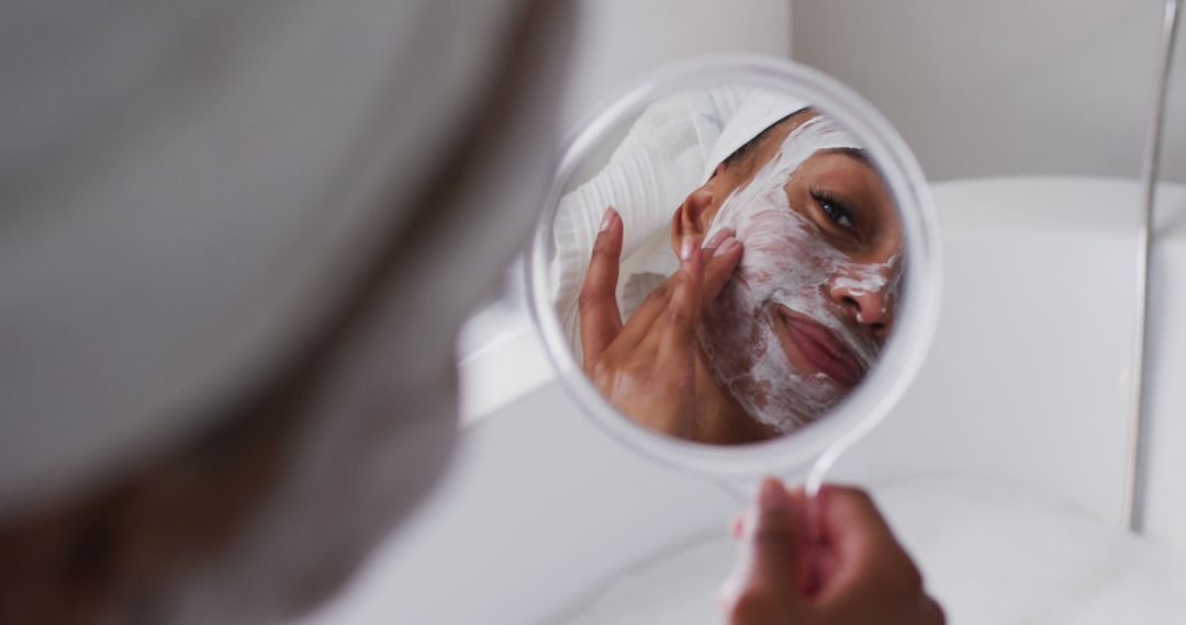 Woman Applying Face Mask While Observing Reflection in Mirror