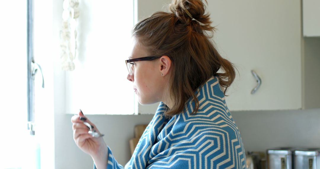 Woman in Kitchen Wrapped in Blue Patterned Blanket Drinking From Spoon - Free Images, Stock Photos and Pictures on Pikwizard.com