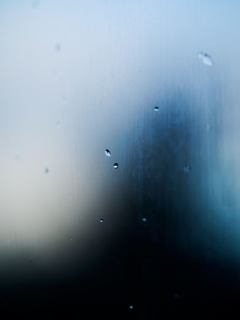 Close-up water droplets on window reflecting blue sky and dark silhouette - Free Images, Stock Photos and Pictures on Pikwizard.com