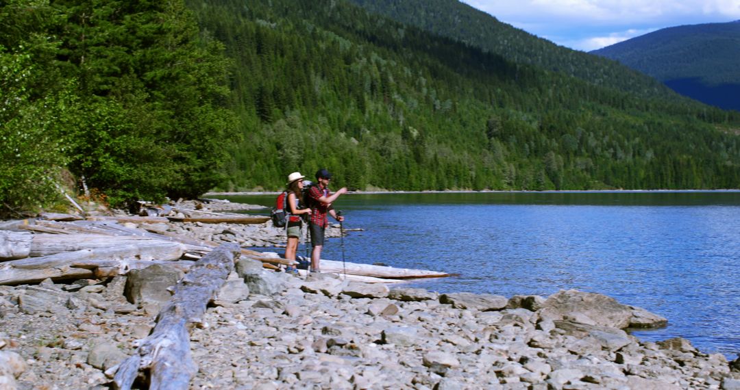Hikers Pausing by Scenic Lakeshore in Forested Mountain Landscape