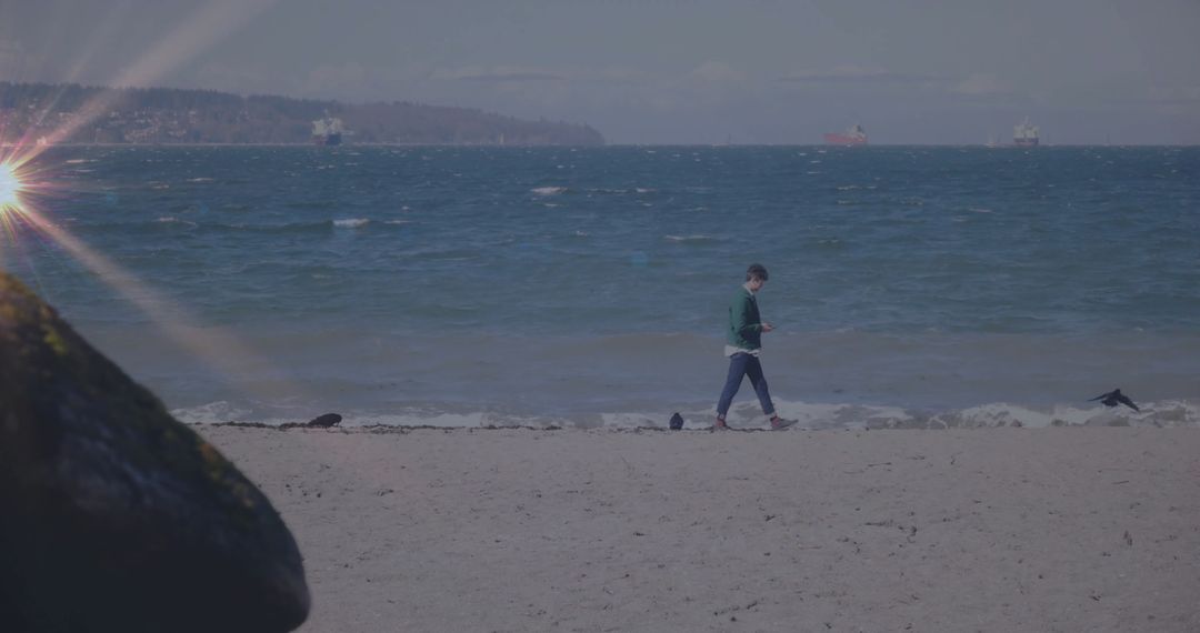Man Walking on Sandy Beach with Smartphone and Ocean Views
