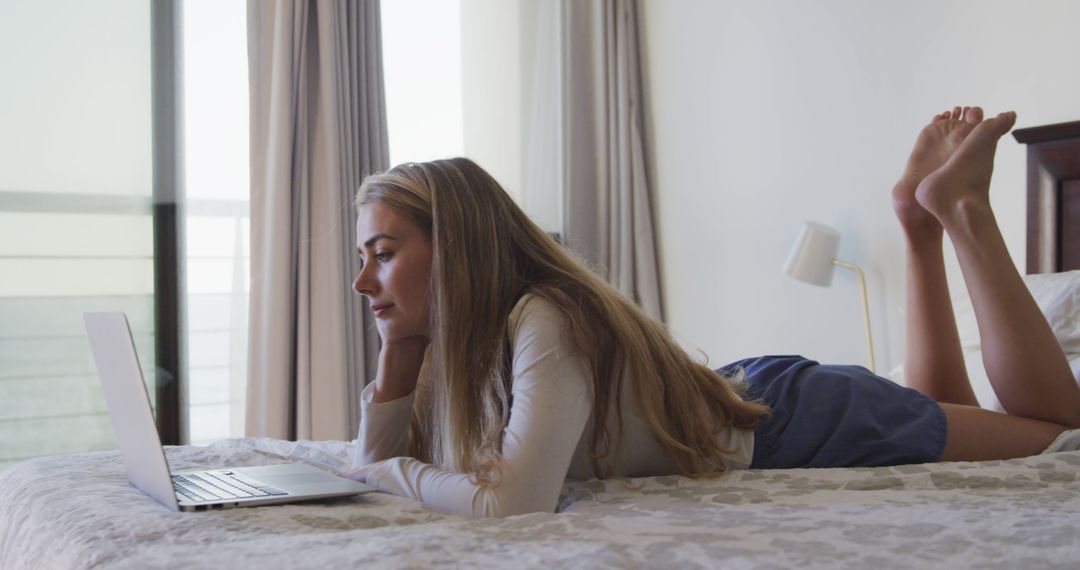 Young Woman Lying on Bed Using Laptop in Bright Room - Free Images, Stock Photos and Pictures on Pikwizard.com