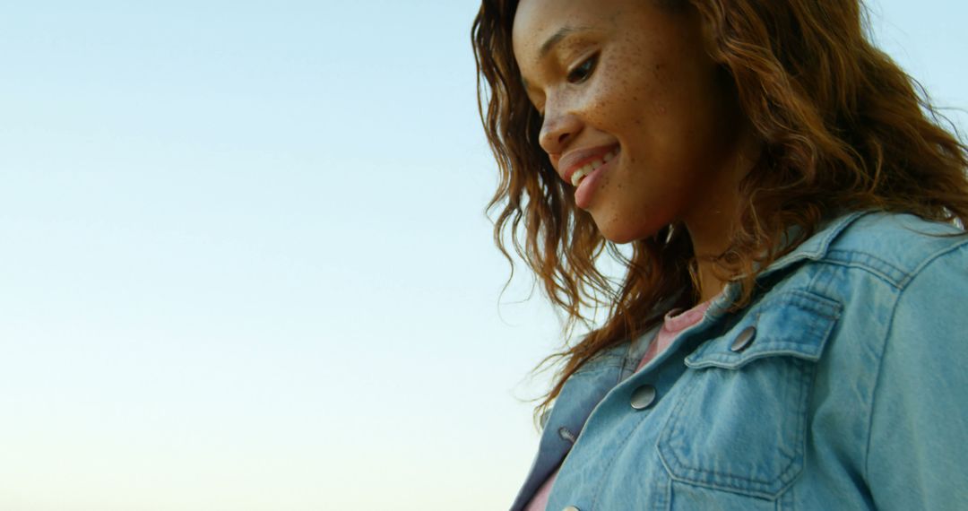 Young woman smiling in sunlight wearing denim jacket - Free Images, Stock Photos and Pictures on Pikwizard.com