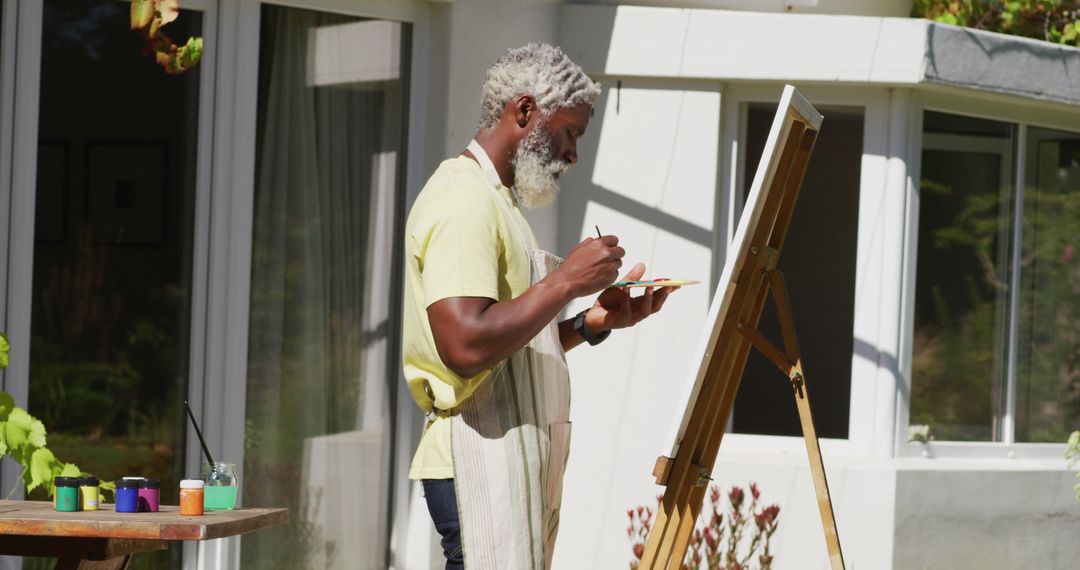 Senior african american man painting picture on a canvas in sunny garden - Free Images, Stock Photos and Pictures on Pikwizard.com