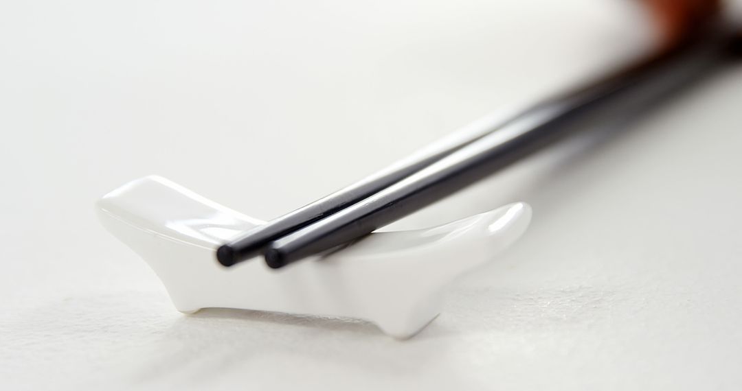 A pair of black chopsticks rests on a white chopstick holder, with copy space - Free Images, Stock Photos and Pictures on Pikwizard.com