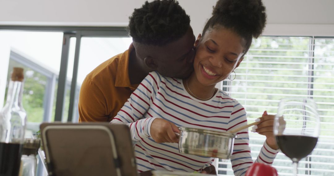 Image of happy african american couple embracing while cooking together in kitchen - Free Images, Stock Photos and Pictures on Pikwizard.com