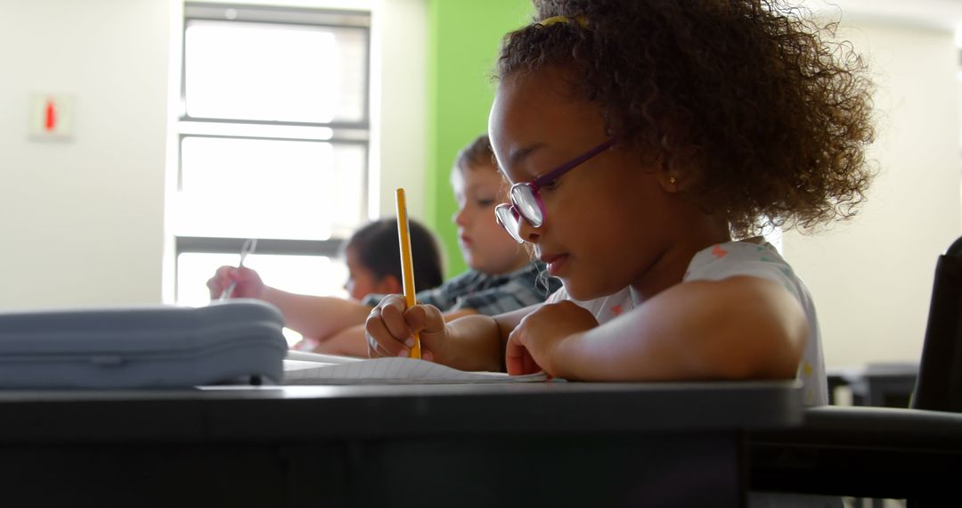 Focused Schoolgirl Writing in Notebook at Classroom Desk