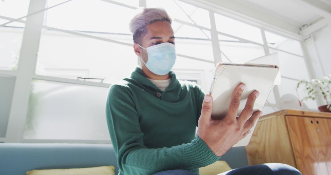 Young Man Wearing Face Mask Using Digital Tablet Indoors - Free Images, Stock Photos and Pictures on Pikwizard.com