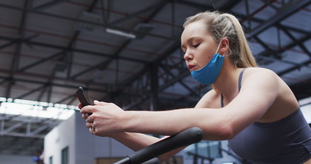 Young woman checking phone while exercising at gym, wearing protective mask - Free Images, Stock Photos and Pictures on Pikwizard.com