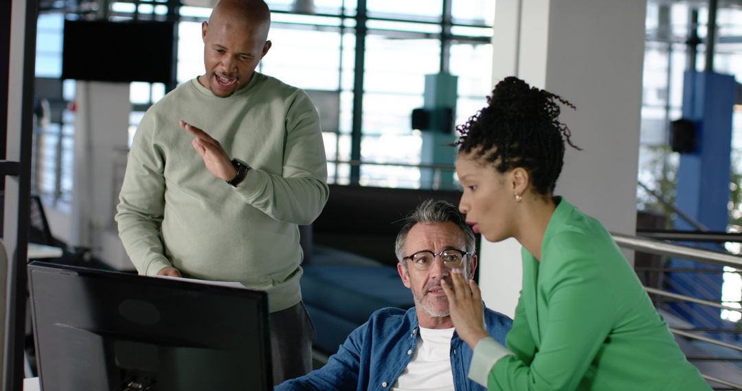 Multicultural team collaborating at open-plan office desk with monitor and bright daylight