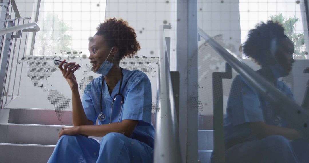 Nurse recording smartphone voice note while resting on hospital stairs with stethoscope
