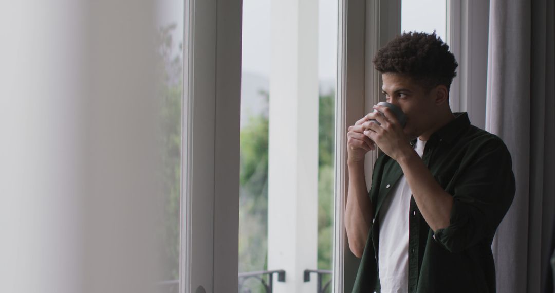 Thoughtful biracial man looking through the window and drinking coffee - Free Images, Stock Photos and Pictures on Pikwizard.com