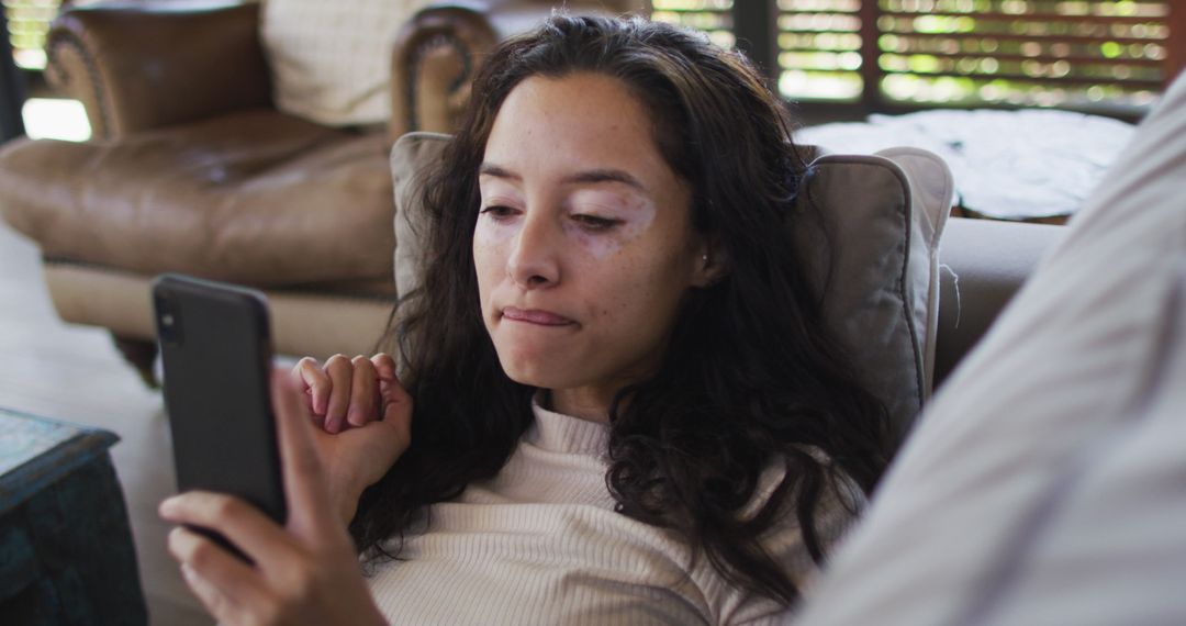Thoughtful Young Woman Lying on Sofa Using Smartphone at Home