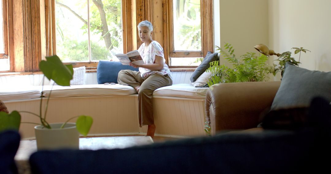 Senior Woman Reading and Relaxing by Sunlit Home Window