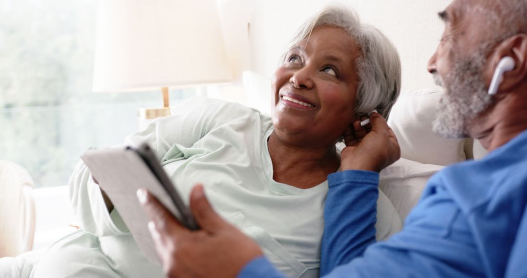 Senior Couple Relaxing with Tablet and Earphones in Comfortable Bed