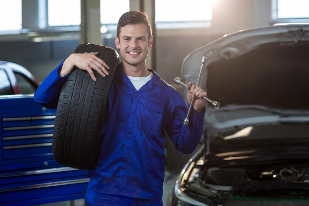 Smiling Mechanic Holding Tire and Wrench in Auto Repair Shop - Free Images, Stock Photos and Pictures on Pikwizard.com