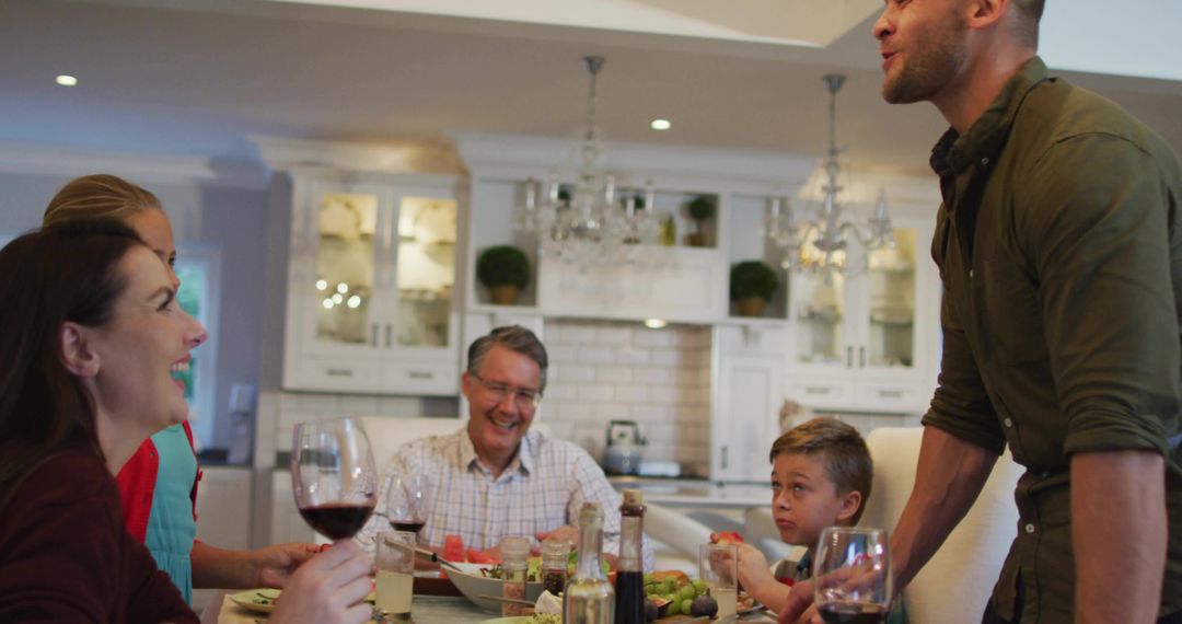 Multigenerational Family Sharing Dinner Around Kitchen Table, Laughing and Toasting Together
