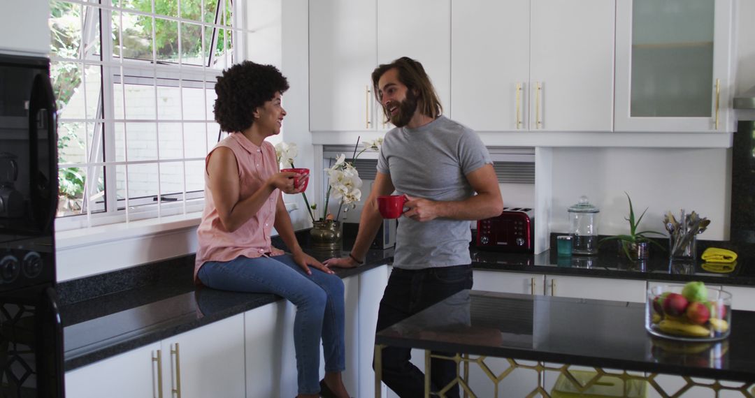 Biracial couple holding coffee cup talking to each other in the kitchen at home - Free Images, Stock Photos and Pictures on Pikwizard.com