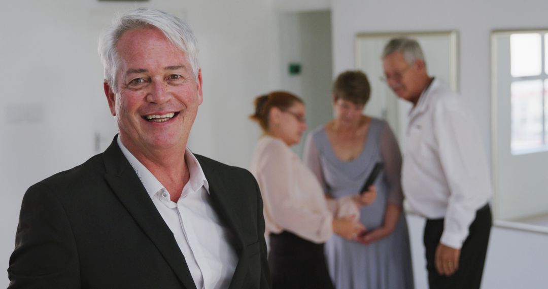 Senior Businessman Smiling at Camera with Colleagues in Background - Free Images, Stock Photos and Pictures on Pikwizard.com