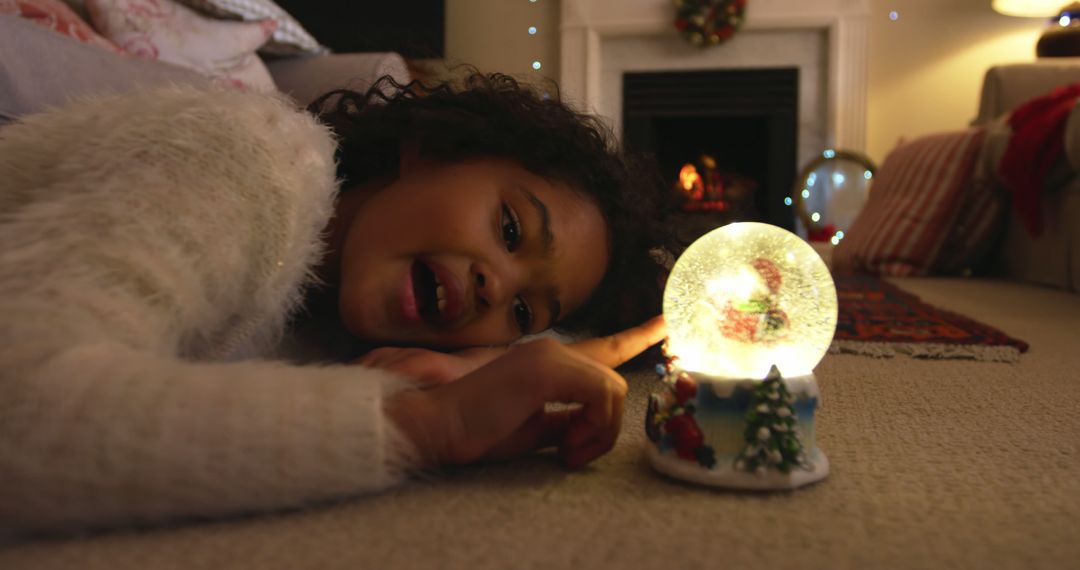 Smiling Child Admiring Christmas Snow Globe Indoors - Free Images, Stock Photos and Pictures on Pikwizard.com